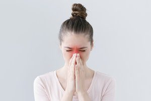 Closeup of young European female isolated on gray background looking stressed, putting hands together as if she is praying with closed eyes to overcome depression and find solution to problem.