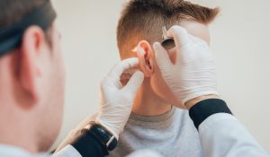 Doctor examines boy ear with otoscope.