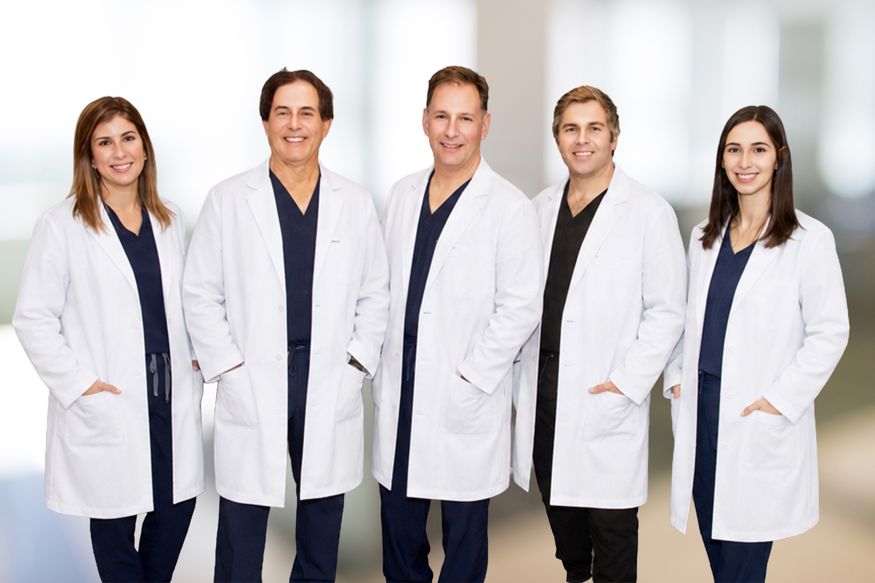 Five doctors in white coats stand together in a bright hallway, smiling at the camera, ready to assist patients.